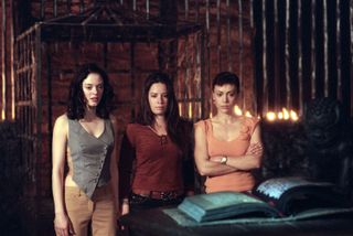 the halliwell sisters stand before a spell book in a still from charmed