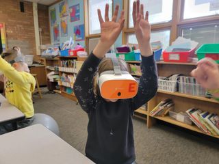 A student with a virtual reality headset on raises their hands while enjoying the VR experience.
