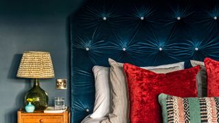 blue velvet headboard with red cushions and green lamp next to it