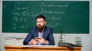 Teacher using a smartphone at his desk with blackboard behind