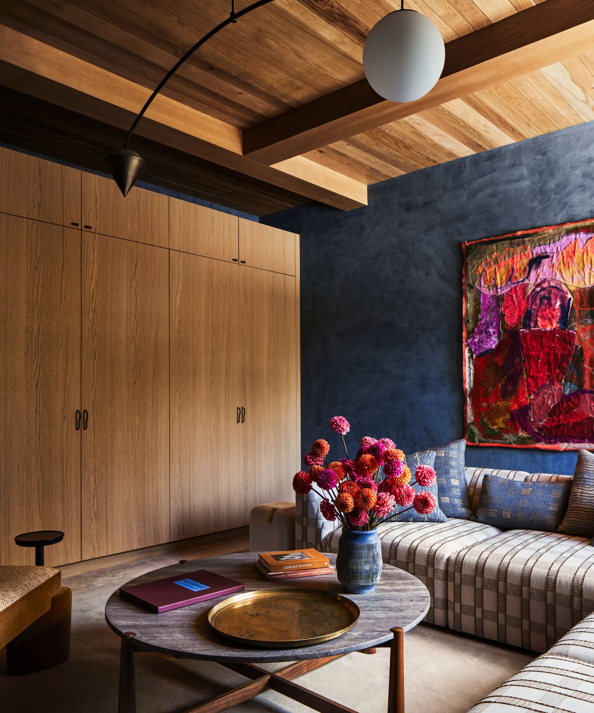 modern living room with wood-clad walls and ceiling, dark blue lime-wash accent wall, large corner sofa, and bright pink artwork on the wall