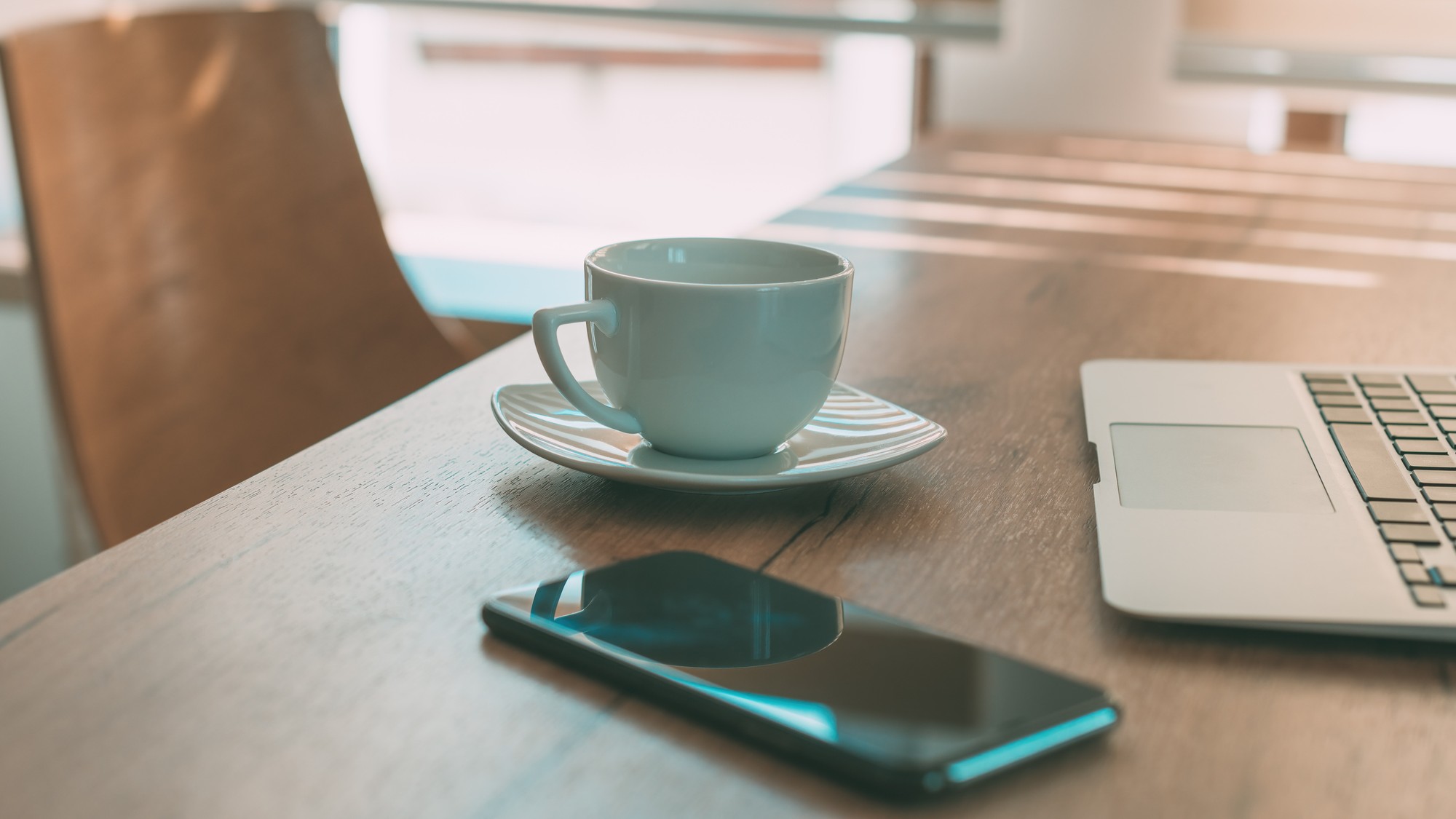 Coffee cup, cell phone and laptop on table