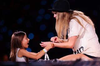 A young fan exchanges friendship bracelets with Taylor Swift as she performs onstage during 