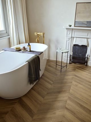 A bathroom with a standing bath and herringbone wood effect floor tiles