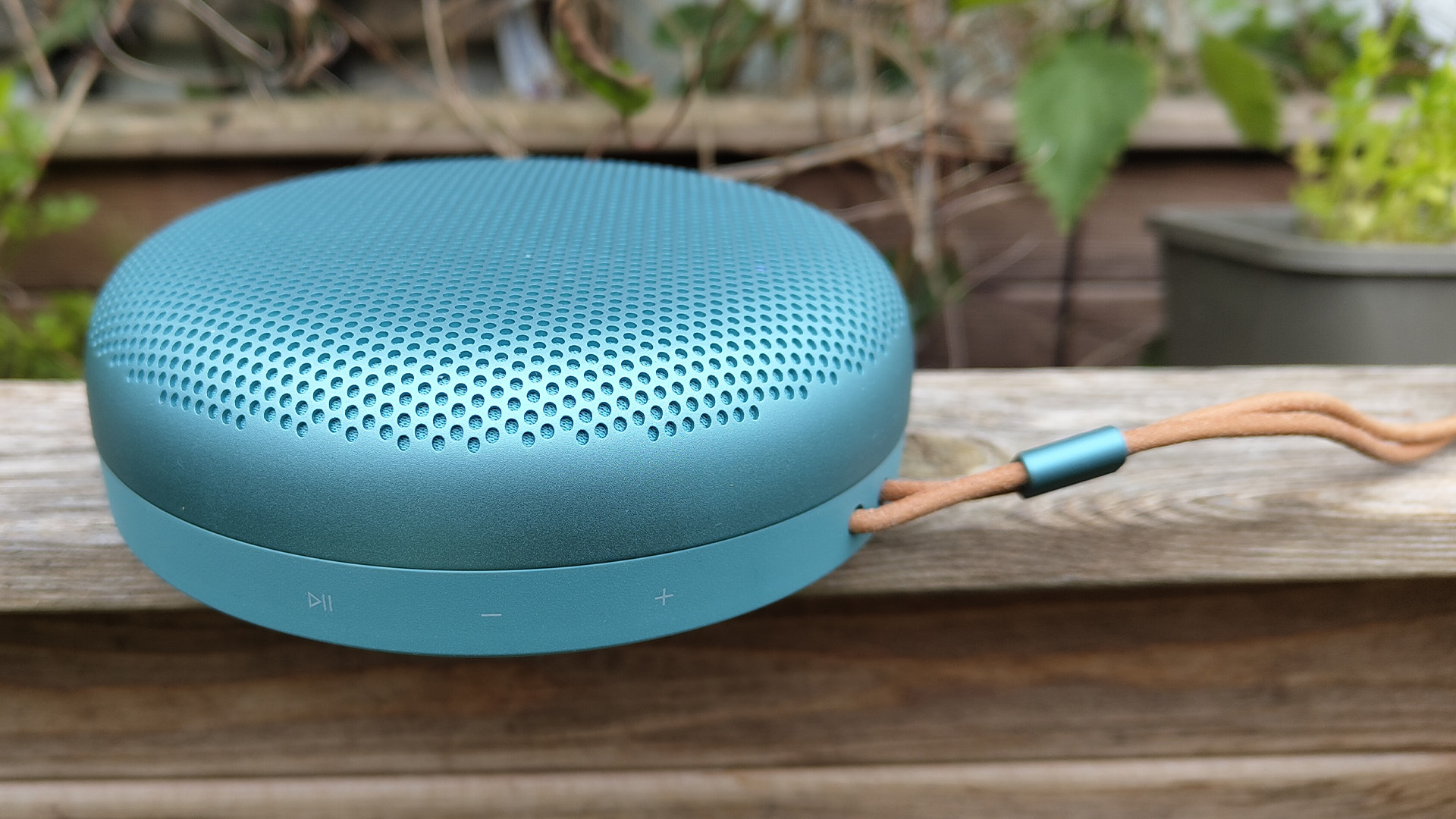 Bang & Olufsen Beosound A1 (3rd Generation) wireless speaker on wooden garden furniture with plants in background