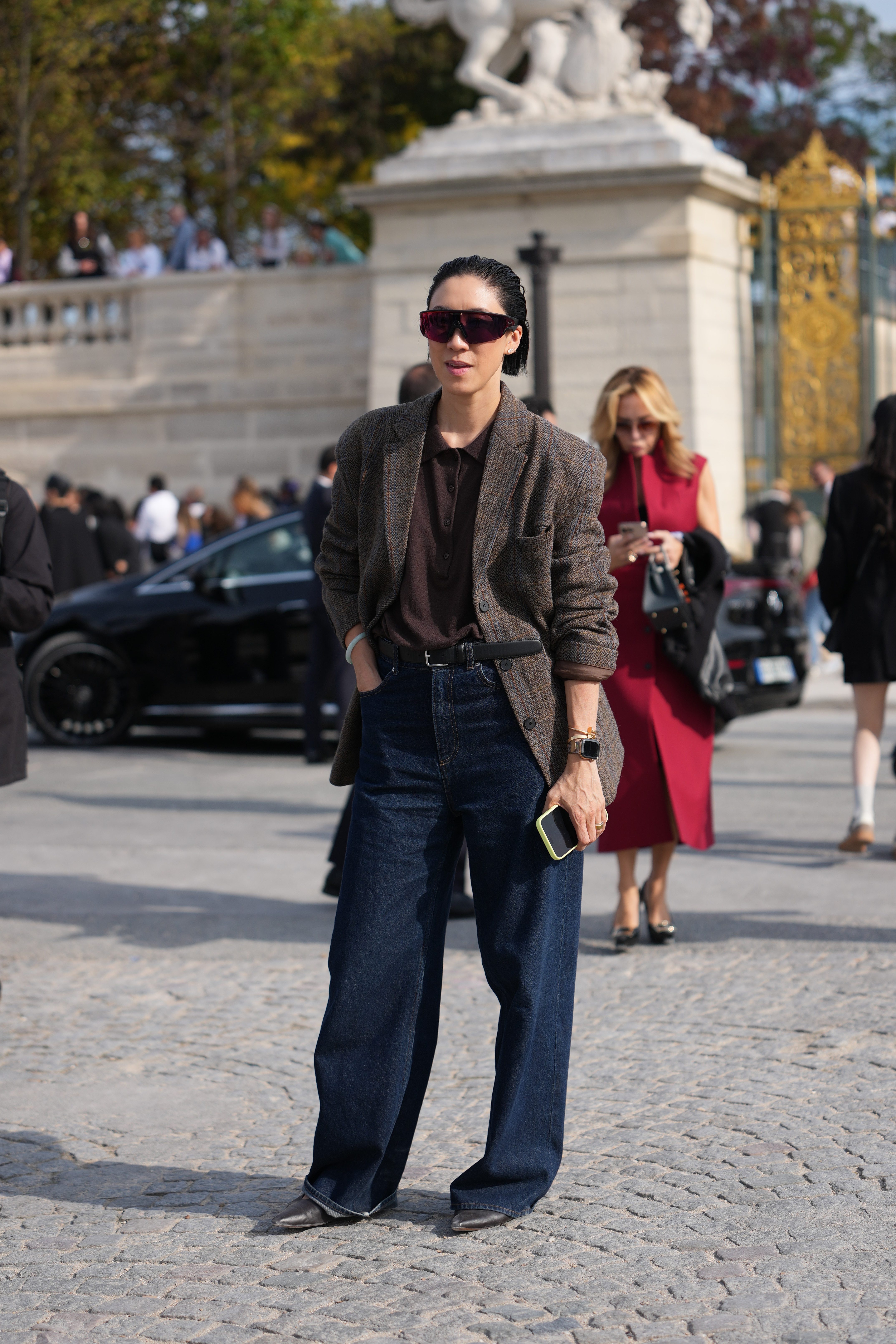 PARIS, FRANCE - OCTOBER 01: A guest wears short slicked-back black hair, oversized dark burgundy shield sunglasses, a gold-tone watch, a brown tweed blazer jacket with a check over a dark brown polo shirt tucked into high-waisted dark indigo wide-leg denim jeans with a black leather belt, and black leather pointed-toe shoes, outside Dior, during Paris Fashion Week - Womenswear Spring Summer 2026, on October 01, 2025 in Paris, France (Photo by Edward Berthelot/Getty Images)