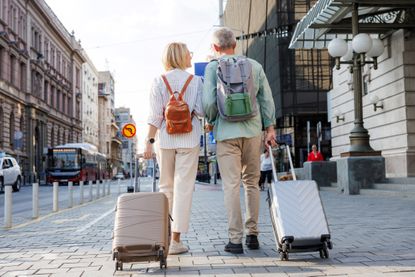 A senior couple walking down a street with luggage.