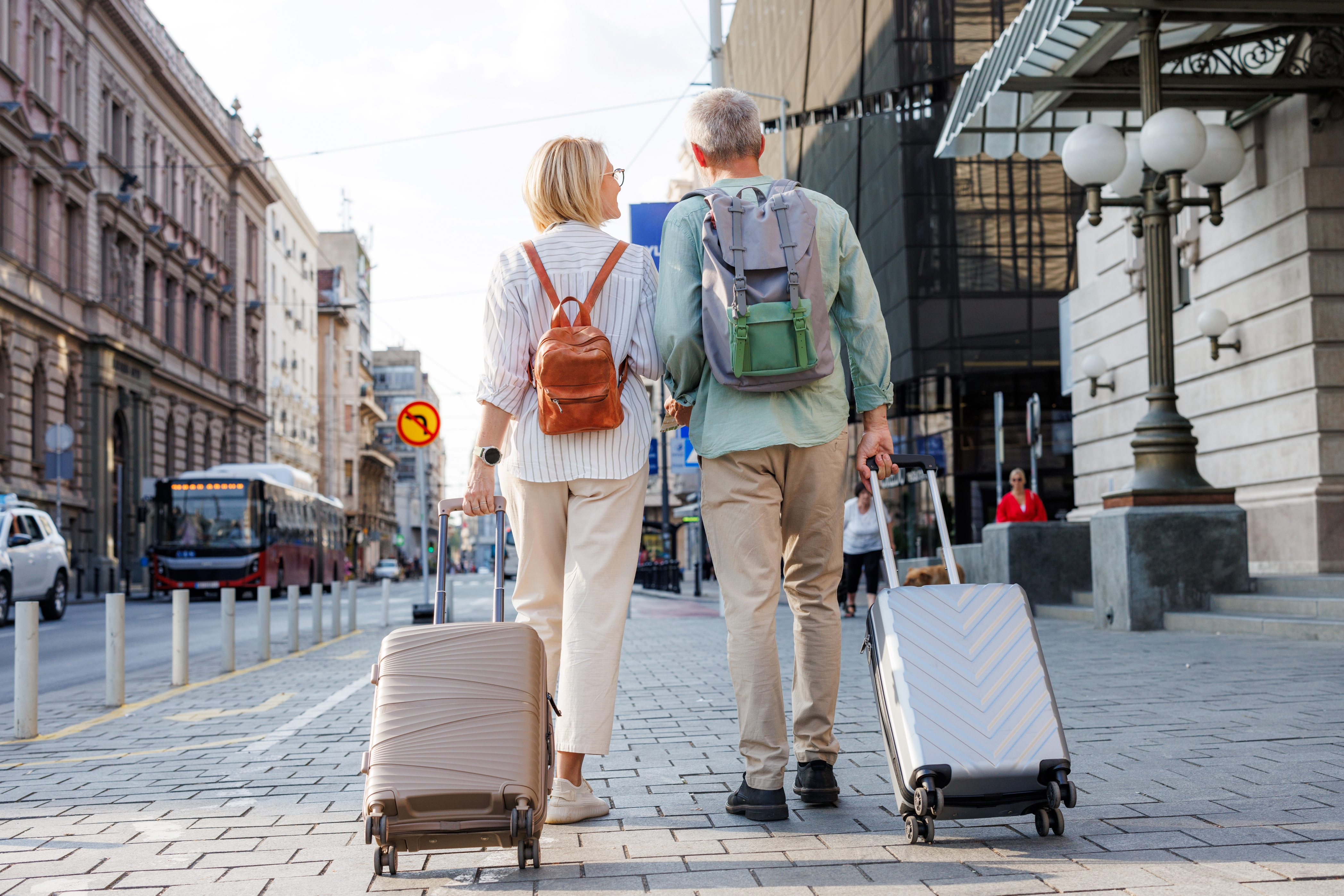 A senior couple walking down a street with luggage.