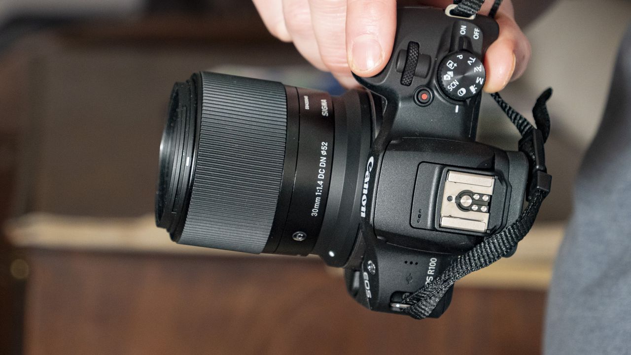 Sigma 30mm F1.4 DC DN Contemporary lens in the hand attached to a Canon EOS R100