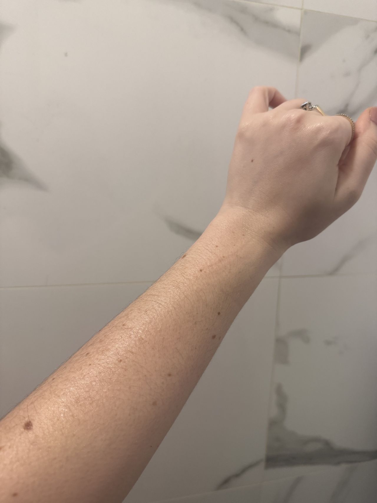Brooke knappenberger arm held up against marble wall after applying phlur vanilla skin body oil