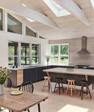 dark gray raw wood cabinets with wooden aspects, vaulted ceiling, shiplap, open plan style, stools, table, view outside