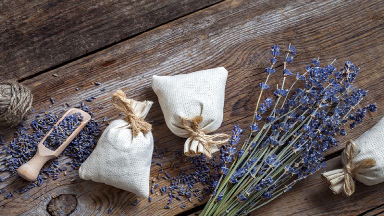 Lavender pillows next to springs of lavender on a wooden table