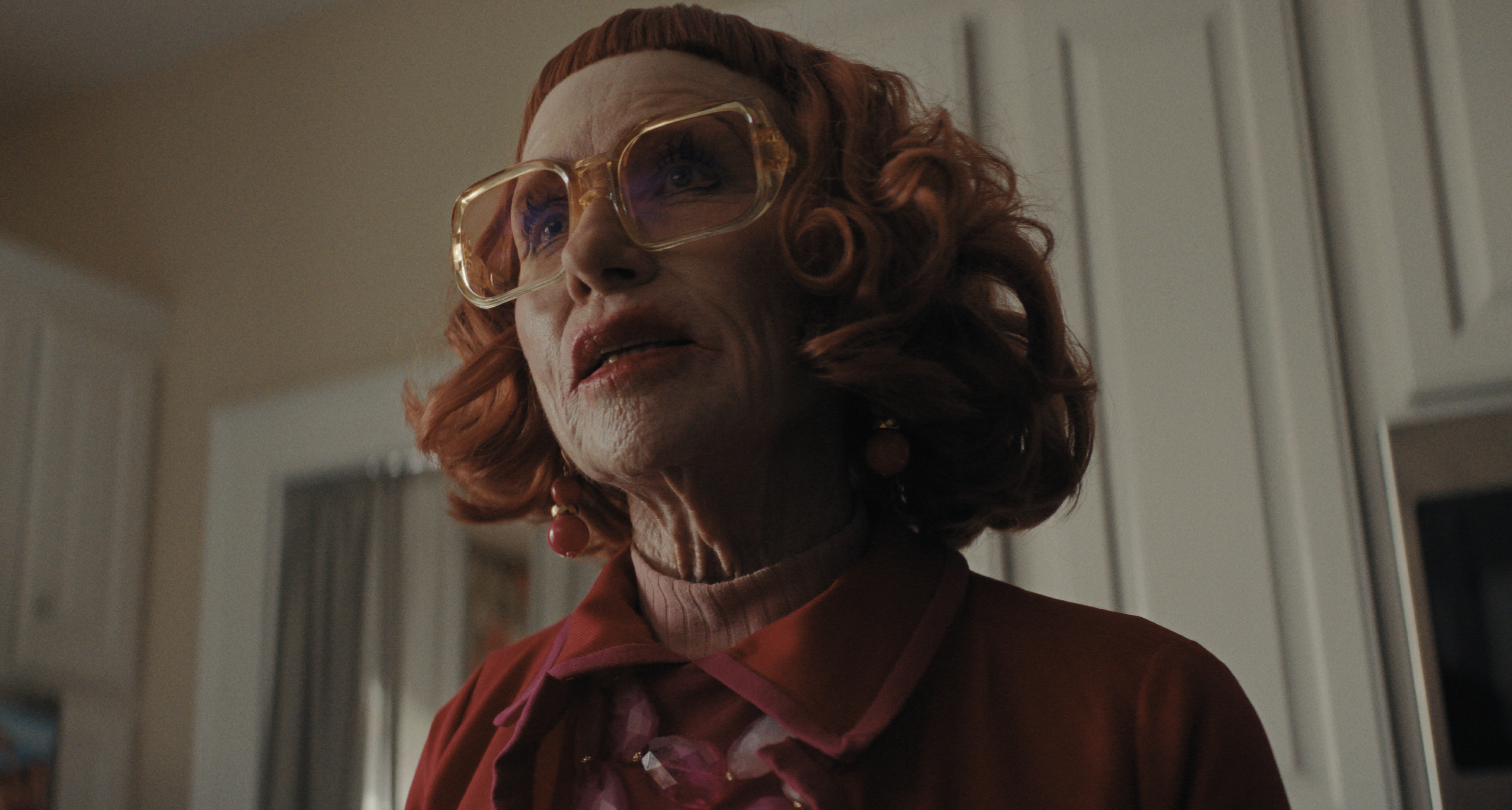 amy madigan as aunt gladys wearing a red jacket and big clear glasses in a still from weapons