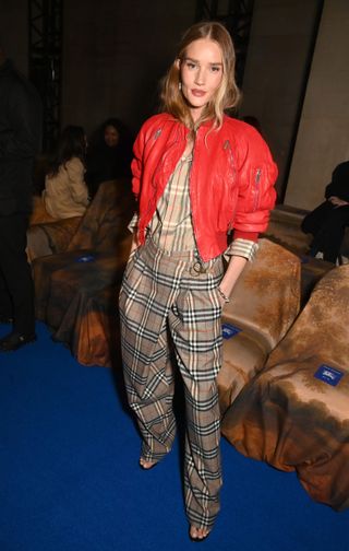 Rosie Huntington-Whiteley front row at the Burberry fall/winter 2025 show in London wearing checkered trousers, a checkered shirt, and a red leather bomber jacket.