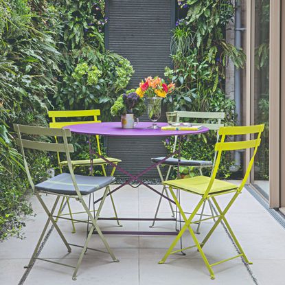 A patio with a purple and green bistro set with vases of flowers