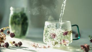 Hot water being into a clear cup with flower buds in a brightly lit room