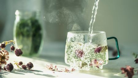 Hot water being into a clear cup with flower buds in a brightly lit room