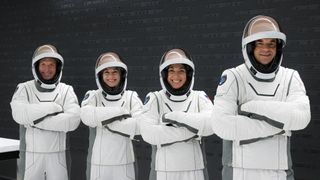 four astronauts in spacesuits with arms crossed and visors up