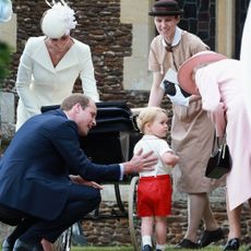 Maria Borrallo wearing a tan nanny uniform smiling at Queen Elizabeth leaning over to greet toddler Prince George and Kate Middleton wearing a white coat and hat bending over a stroller in the background