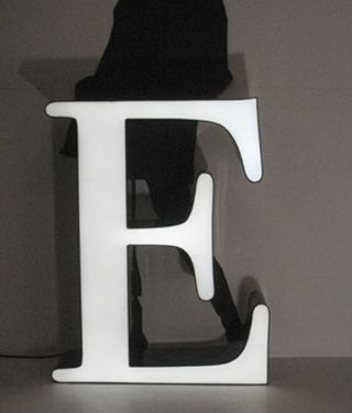 A silhouette of a person standing behind a large lit up "E" on the ground in front of them.