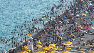 A crowded beach with lots of people swimming in the sea