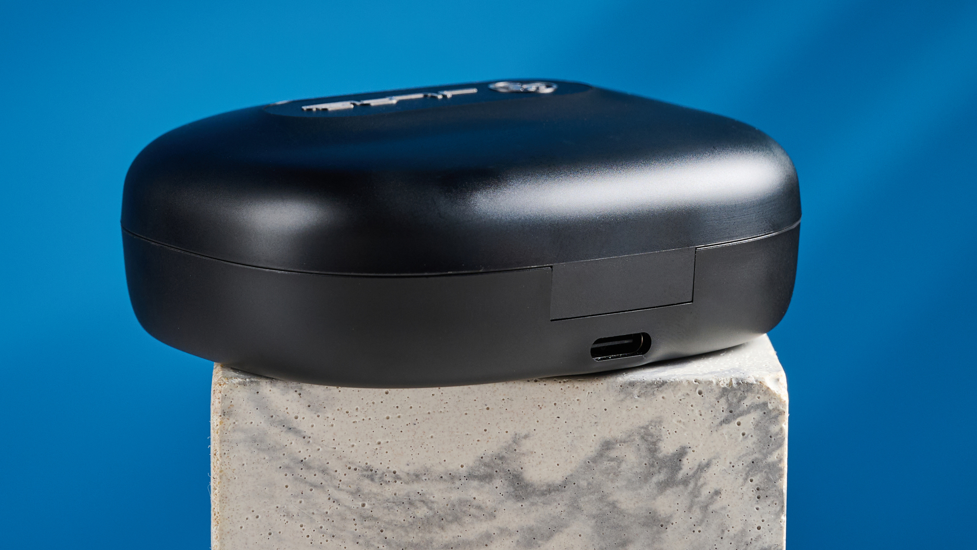 Jlab epic open sport open-earbuds in a black colorway photographed on a blue background.