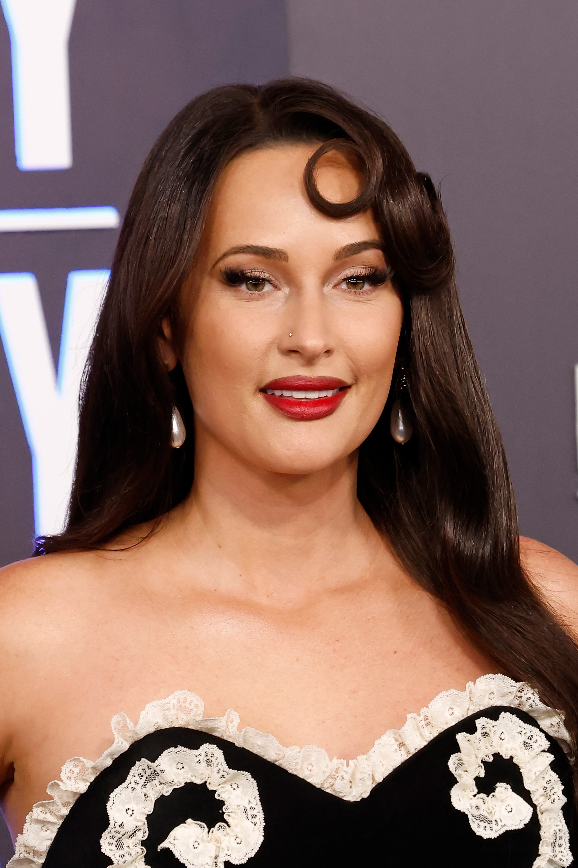 a white woman with dark hair poses on the red carpet at the academy of country music awards