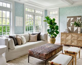 Bright living room with blue walls, cream sofa, white side table, green plant, upholstered ottoman