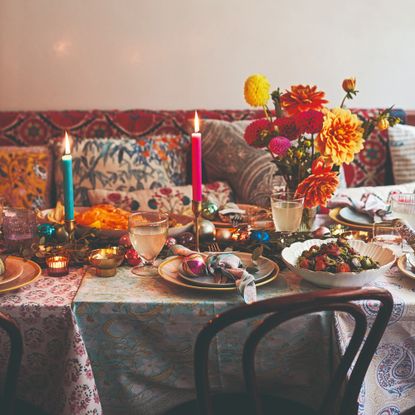 A dining table with a banquet seating covered in colourful printed tablecloths and sharing platters