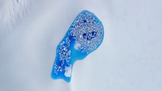 An aerial photo of a vibrant pond of blue water surrounded by snow