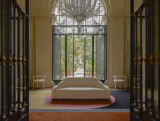 A palatial hotel's lobby features colorful carpet, a vintage-style white upholstered sofa, and a monumental Murano glass chandelier.