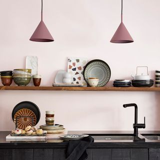 A dark kitchen with one long open shelf with kitchen accessories, crockery and other utensils above a sink