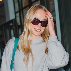 Sophie Turner wearing a gray hoodie, navy sweatpants, and navy Puma sneakers