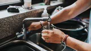 a person fills up a glass of water from the tap