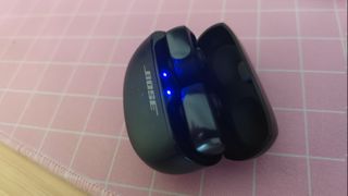 Bose Ultra OpenEarbuds in an open case with blue LEDS indiccating that they're in Bluetooth pairing mode