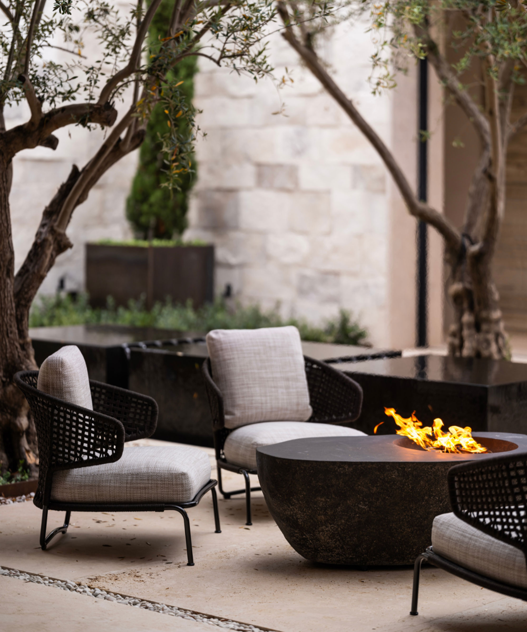 modern fire table with garden chairs on a patio surrounded by trees