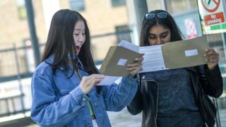 Two female students with shocked expressions reading letters outside of a building