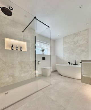 minimalistic bathroom with large wall and floor tiles with subtle marble effects, large walk in shower, freestanding bath, back to wall toilet