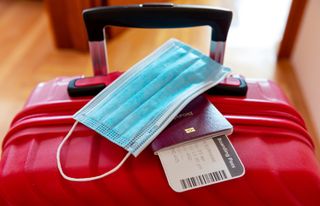 Face protection mask and travel documents over suitcase.