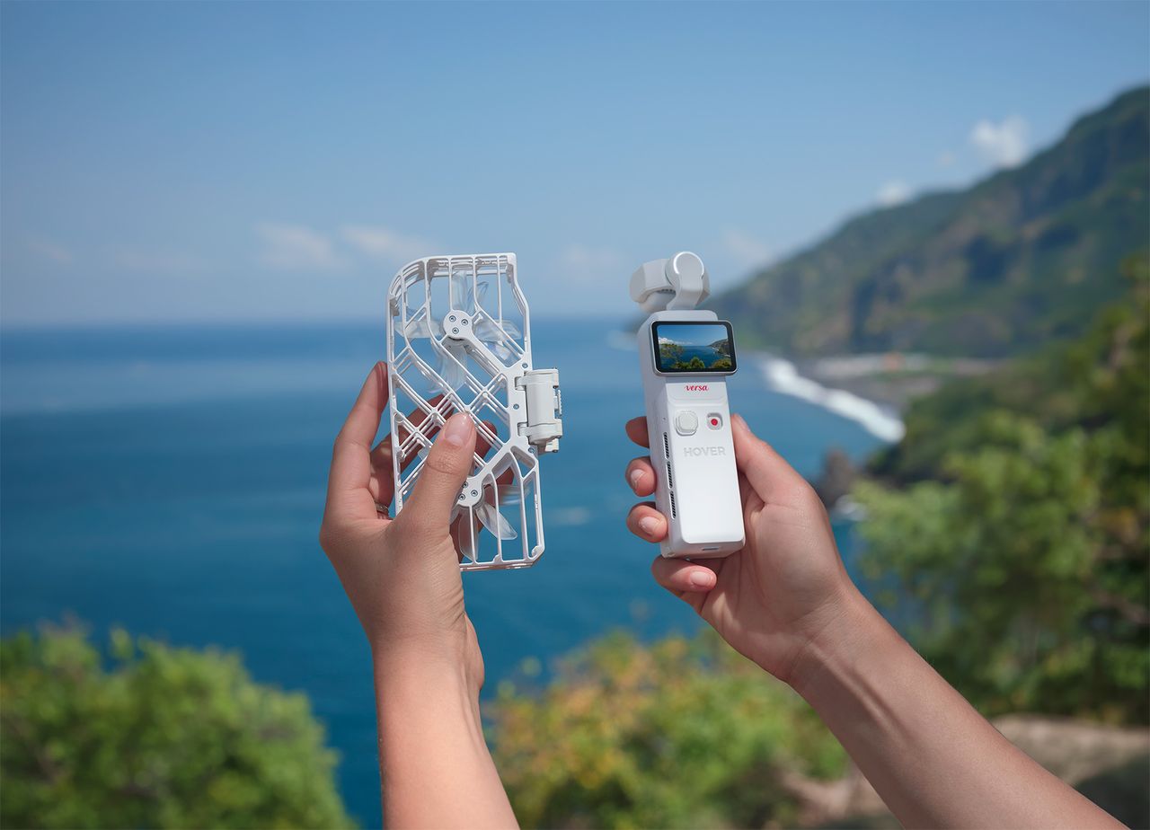 HoverAir Versa 2-in-1 drone and pocket gimbal camera in white, the two components are apart and in person's hands, by a dramatic coastline on a sunny day