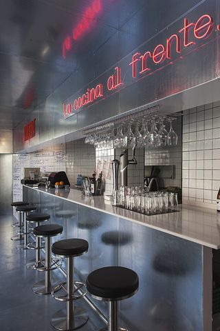 metal bar and red sign with 'la cocina al frente'. white tiles on wall behind bar
