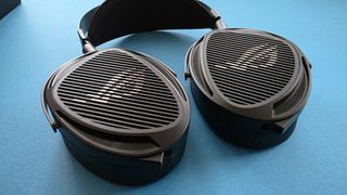 A pair of large, black, over-ear headphones with a striped grille design rests on a blue surface.