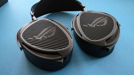 A pair of large, black, over-ear headphones with a striped grille design rests on a blue surface.