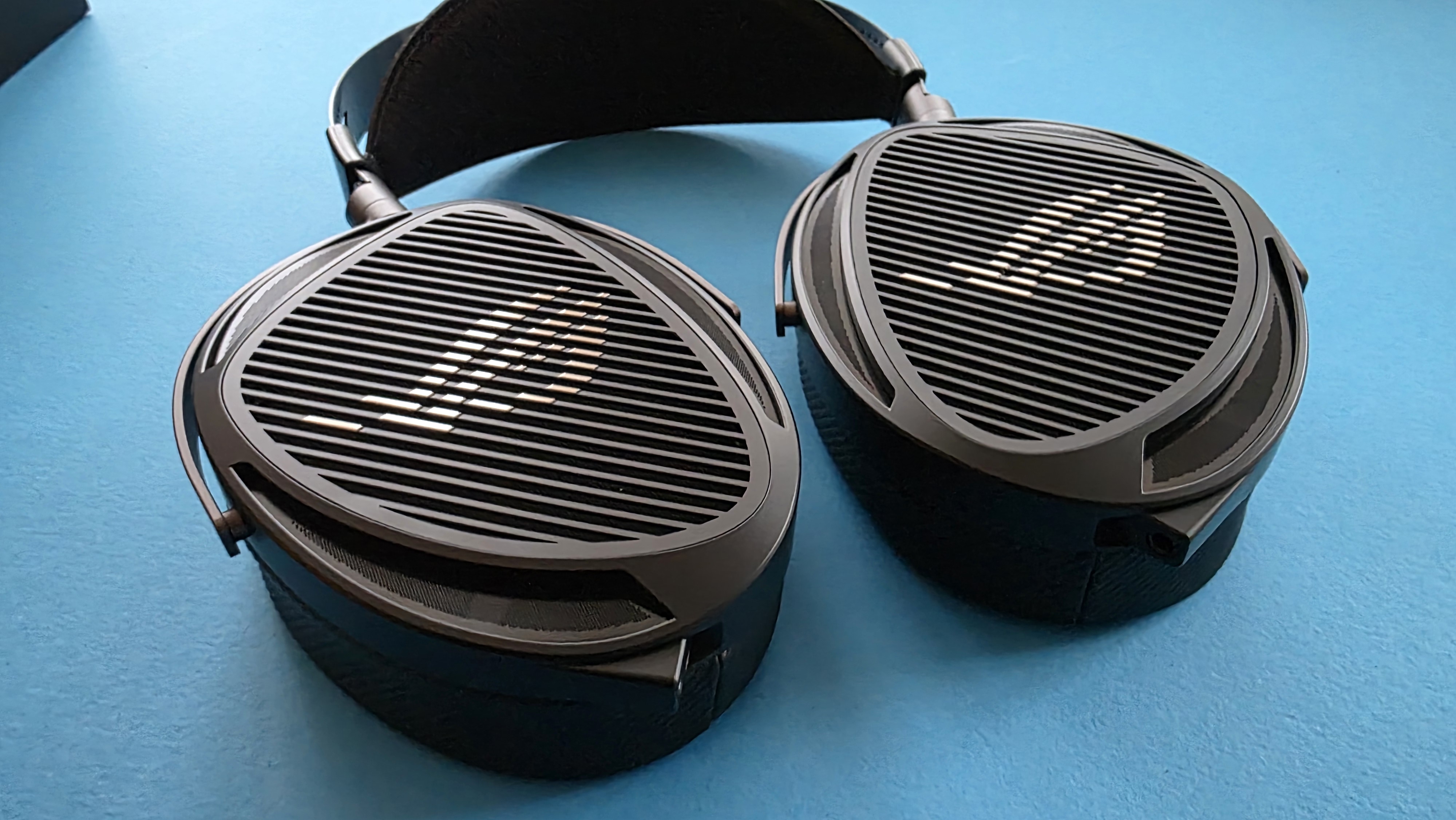 A pair of large, black, over-ear headphones with a striped grille design rests on a blue surface.