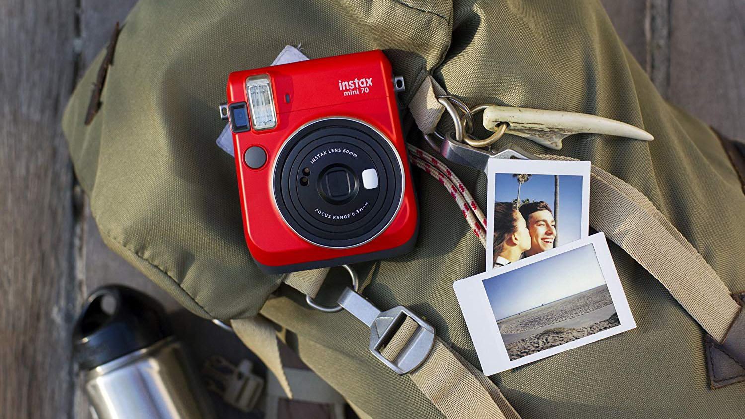 En röd Fujifilm Instax Mini 70 på en ryggsäck, flankerad av två utskrifter