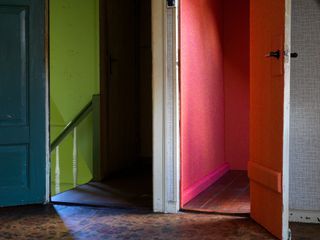 A doorway to a staircase with yellow walls next to a doorway to a room with pink walls.
