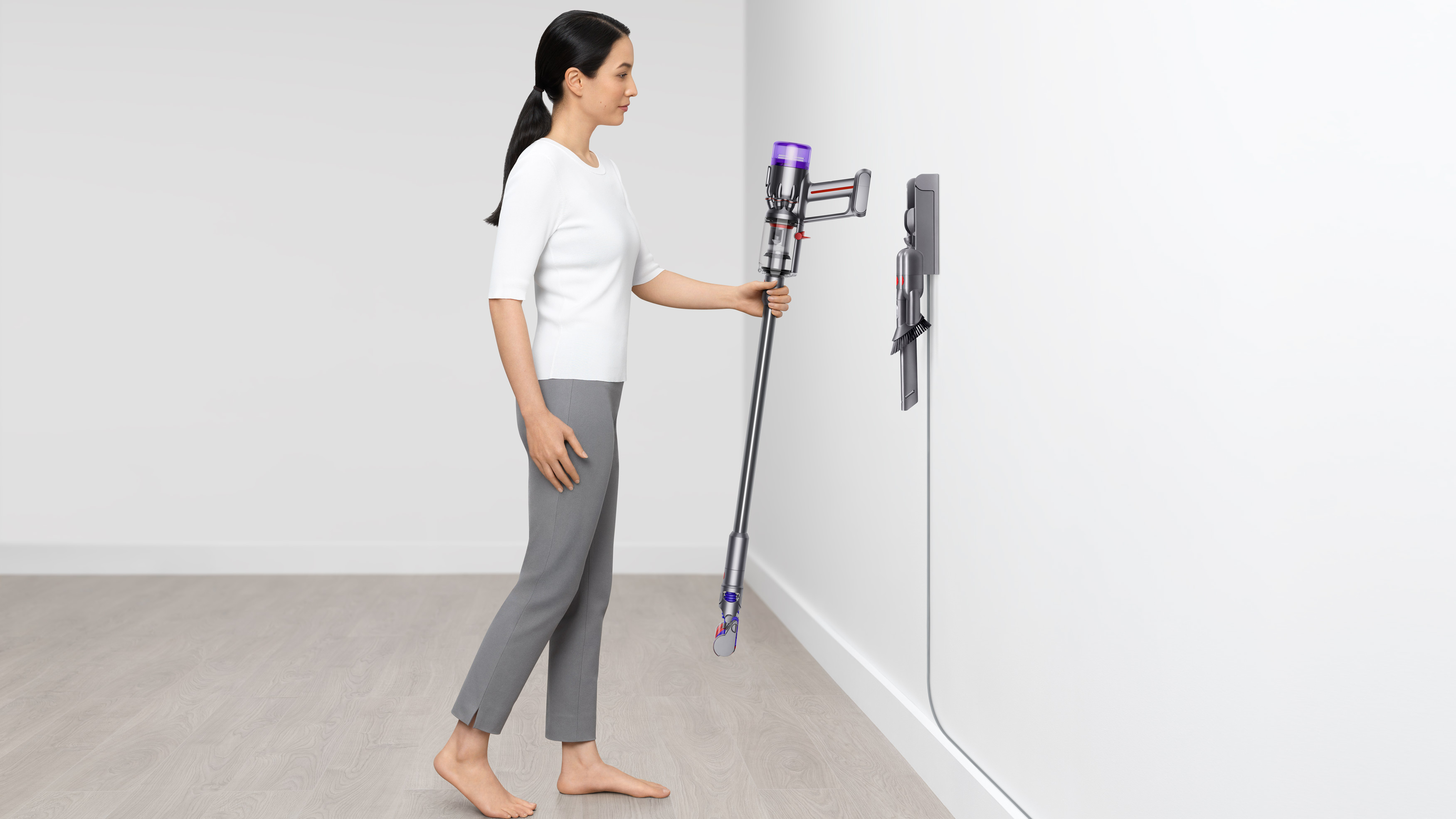 Dyson Micro 1.5kg being hung on the wall charger by a woman