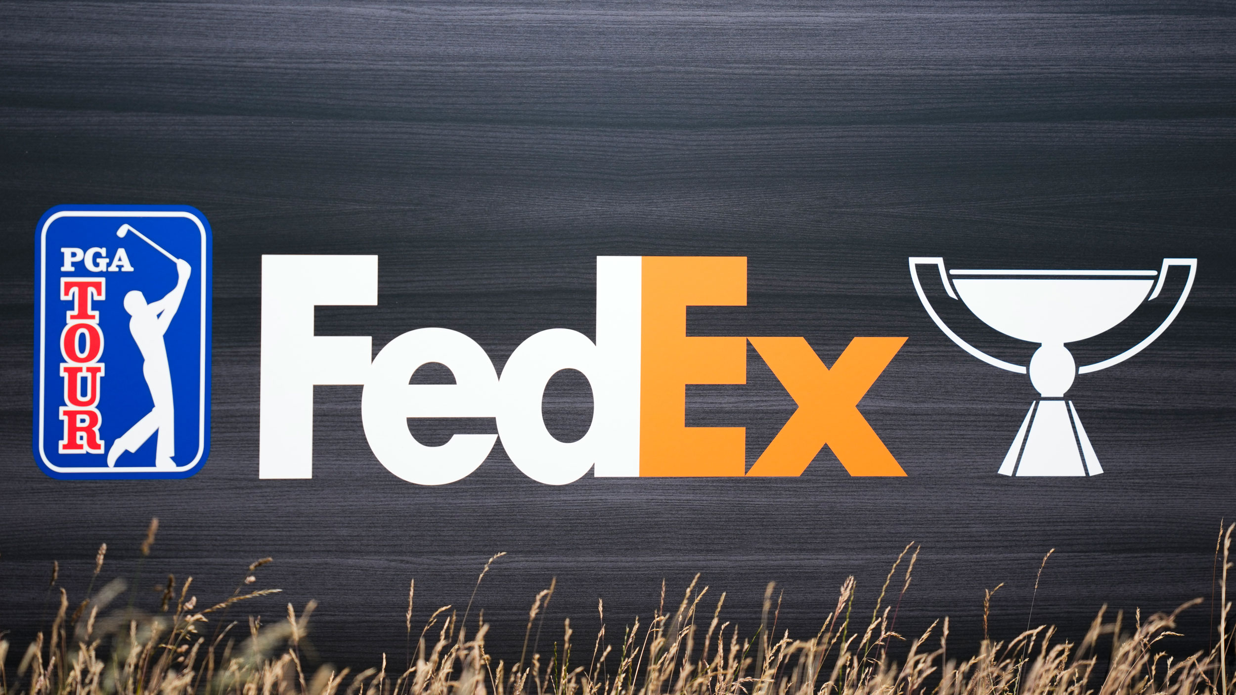 The PGA Tour logo (left) alongside the FedEx logo (centre) and an outline of the FedEx Cup (right) on a slate background
