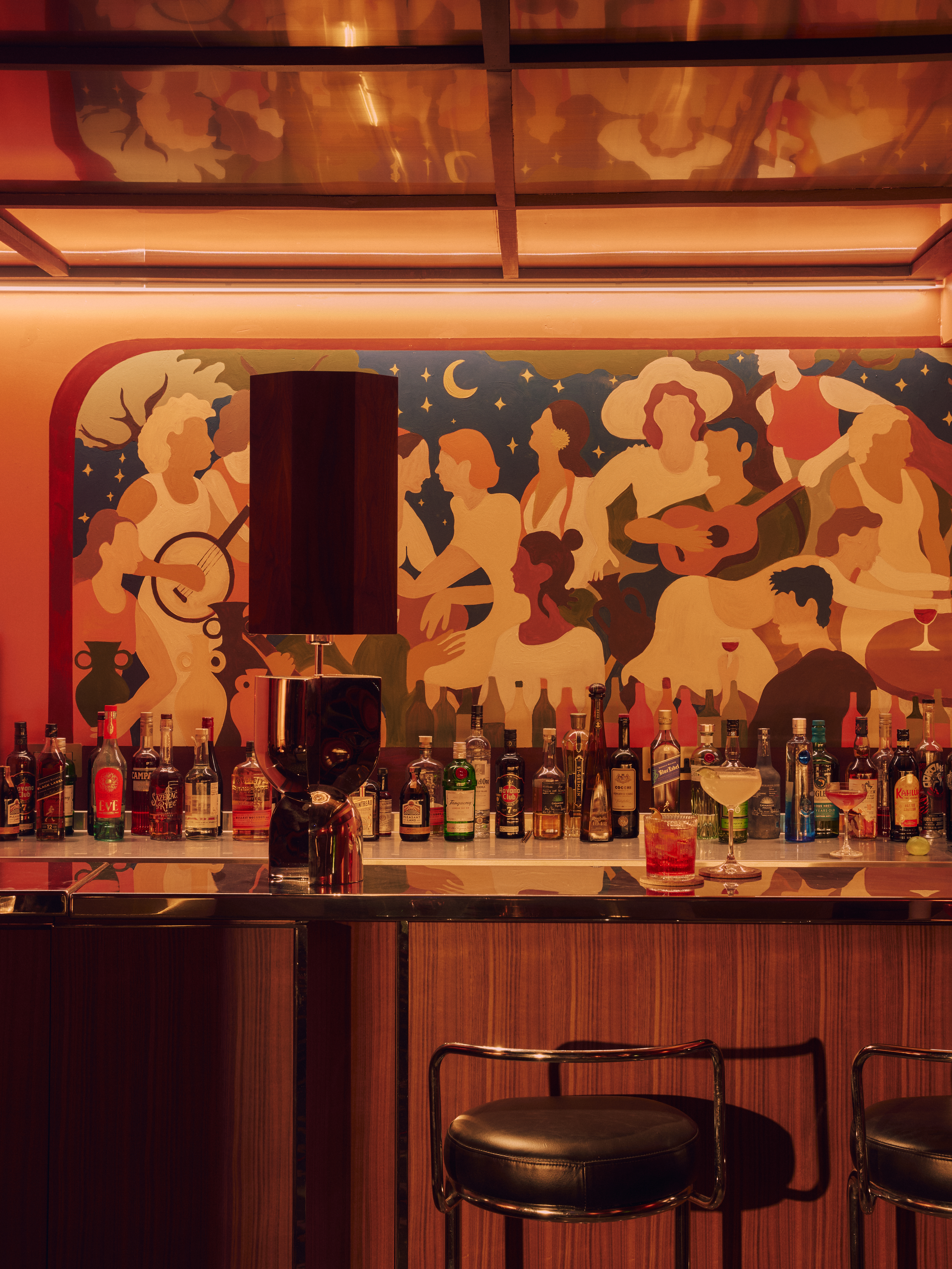 The interior of a private members' club's bar and lounge, decorated with sprawling wall and ceiling murals, earthy tones, plush furniture, and plenty of artworks.
