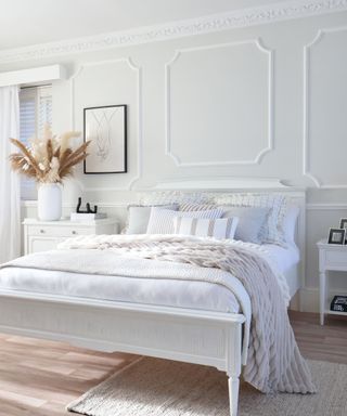 A bedroom with a white bed, light gray walls, and wooden flooring
